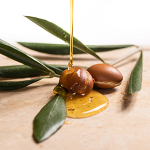 Argan oil being poured over Argan seeds and leaves.