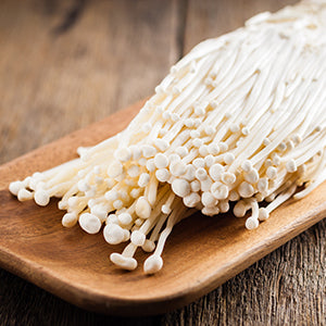 Multiple long thin mushrooms on a wooden bowl over wooden table.